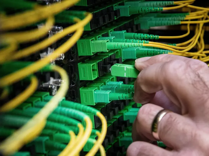 A hand seating an SC/APC connector into a row of green adapters
